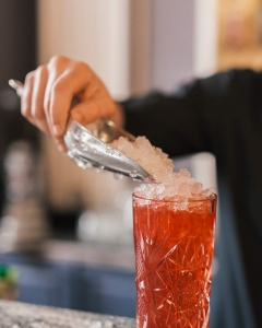man pouring ice into a cocktail drink, sitting at a wet bar in Connecticut