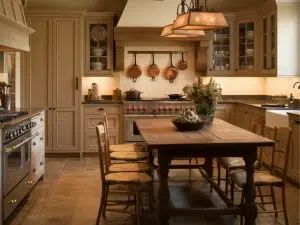French country kitchen that blends elegance with countryside charm. Pearl-white cabinets, exposed wood beams, and gold accented fixtures.