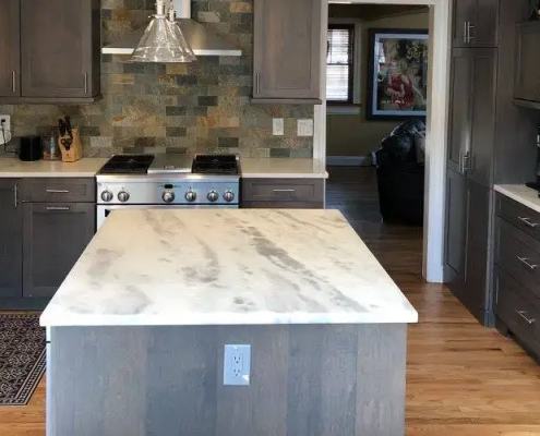 Bright kitchen featuring a grey island with a marble countertop, introducing sleek, low-maintenance design trends.