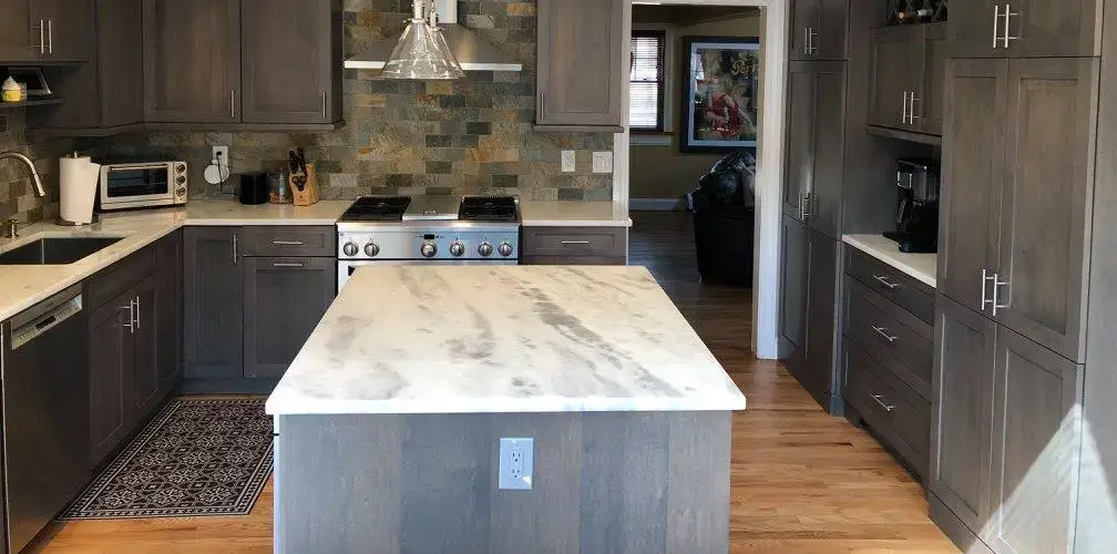 Bright kitchen featuring a grey island with a marble countertop, introducing sleek, low-maintenance design trends.