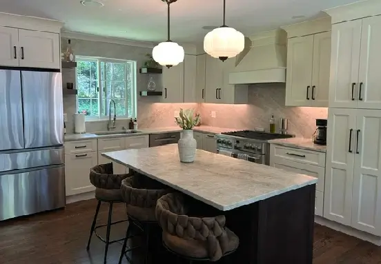Expanded kitchen island layout with a light stone countertop, dark base, and three brown woven bar stools beneath glowing globe pendant lights.