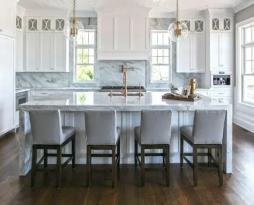 Modern design social hub kitchen island featuring a white marble countertop, four grey bar stools, gold hardware, and elegant pendant lights.
