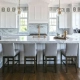 Modern design social hub kitchen island featuring a white marble countertop, four grey bar stools, gold hardware, and elegant pendant lights.