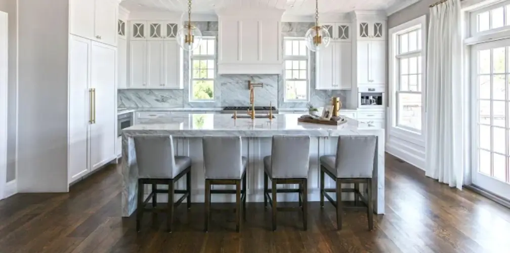 Modern design social hub kitchen island featuring a white marble countertop, four grey bar stools, gold hardware, and elegant pendant lights.
