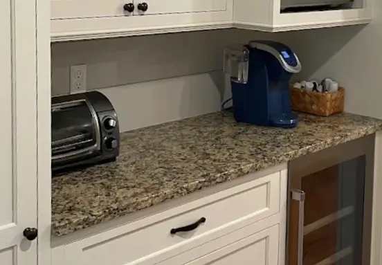 Speckled granite-look countertop in a Connecticut kitchen, tan and black pattern beside a toaster and coffee maker in white cabinetry.