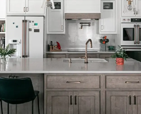 Remodeled Connecticut kitchen island with pale gray engineered stone counter, taupe wood cabinets, gold fixtures, and pendant lighting.