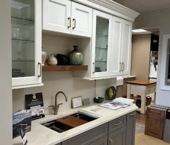 kitchen-bathroom-remodel-challenges Kitchen showroom display with white glass-front upper cabinets, gray lowers and brass pulls, for comparing finishes before a kitchen and bath remodel.